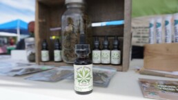 Image of a South Central Hemp Coop tincture bootle sitting on a table at a farmer's market display.